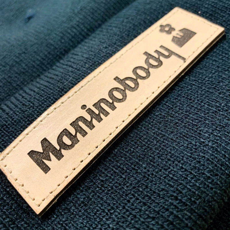 Tan and black Maninobody Lazer cut leather patch on blue garment.